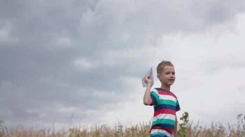 Happy Little Boy Playing With A Paper Airplane In A Field.