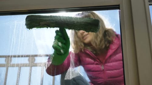Happy Woman in Rubber Gloves Washes Dirty Window with Fur Coat Using Detergent Outside