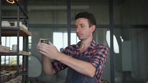 Man Inspecting Pottery in Studio Setting