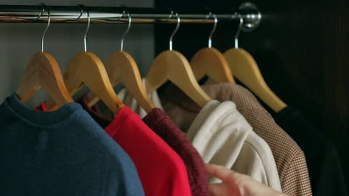 Hand Choosing Clothes from Dark Wood Wardrobe