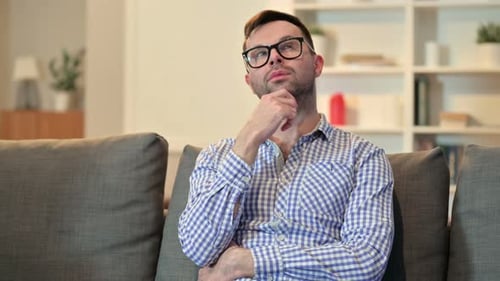 Nachdenklicher junger Mann sitzt zu Hause und denkt
