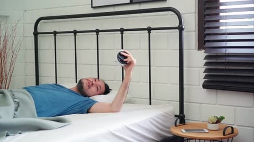 Asiatische Männer schalten den Wecker aus, wenn sie im Bett im Schlafzimmer zu Hause aufgewacht sind