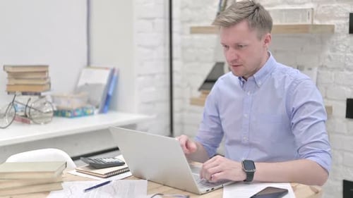 Man Celebrates Success at Laptop in Workplace