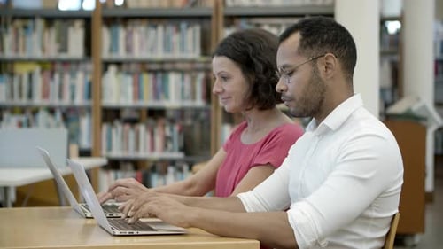 Side View of Colleagues Sitting at Library and Communicating