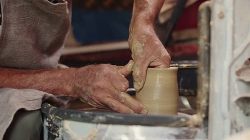 Un potier professionnel en tablier transforme de l'argile sur un tour de potier et donne au produit des parois fines.