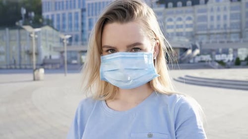 Woman Putting on Surgical Face Mask in City