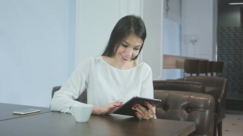 Happy Young Woman Using Digital Tablet in a Coffee Shop