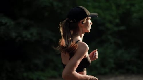 A Young Woman Runner is Listening to Music in Earphones and Training in Summer Forest