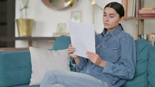 Young Woman Reads Documents on Couch at Home