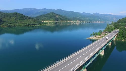Red car driving on bridge over lake