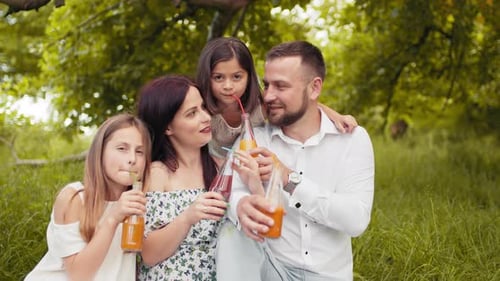 Smiling Father Mother and Two Cute Daughters Drinking Fresh Juice at Green