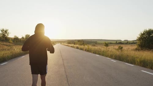 Back View of Male Person Walking to Sunset and Training Kicks on Country Road
