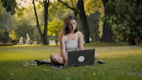Junge Frau arbeitet mit Laptop in einem Park.