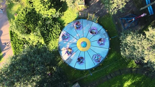 Bright carousel in city park. Family holiday on sunny summer day. Drone footage