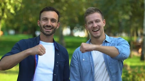 Männliche Freunde stoßen mit Fäusten und lächeln im Freien vor der Kamera, Wahre Freundschaft
