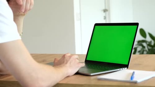 Close-up of a Man Uses Laptop with Green Mock-up Screen While Sitting at the Desk