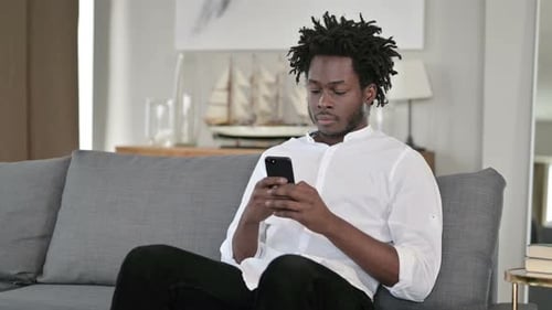 Young Adult Relaxing with Phone on Couch Indoors