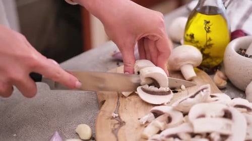 Woman Cuts Champignon Mushrooms with a Knife on a Wooden Cutting Board