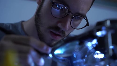 Portrait of Successful Young Bearded Man in Glasses Working with a Soldering Iron at His Working