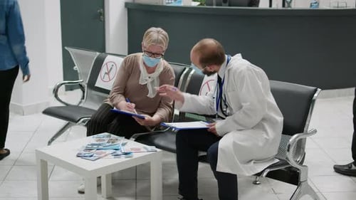 Physician and Senior Woman with Face Masks Talking in Waiting Area