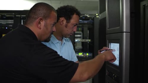 Two men working on monitor in server room