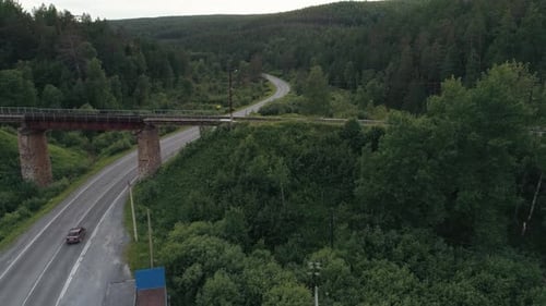 Eine verlassene rostige Eisenbahnbrücke über der geschwungenen Straße mit einem fahrenden LKW
