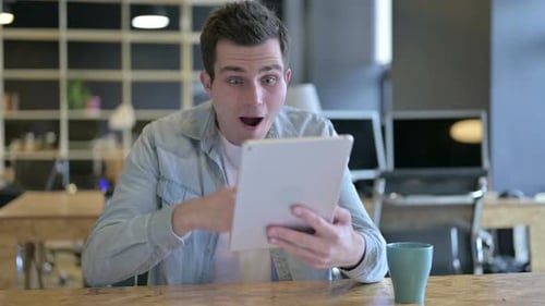 Young Male Designer Celebrating Success on Tablet in Office