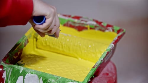 Covering a Roller in Yellow Paint in the Paint Tray