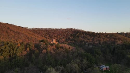 Aerial view around forest covered mountain at sunset with religious shrine tucked into trees.
