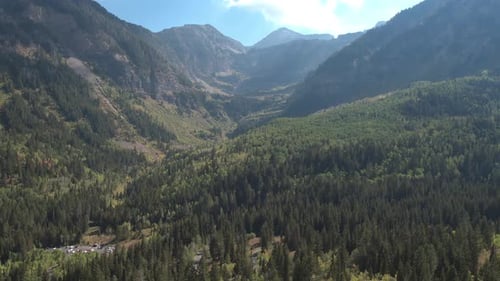 Aerial panning view of green forest stretching across the mountain valley