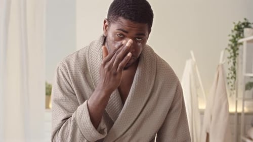 Young Man Applies Lotion to Face in Bathroom