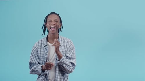 Satisfied black man in a plaid shirt and with dreadlocks dances with joy in the studio