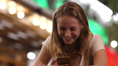 Cheerful Woman at the Bar Reading Funny Messages on Her Mobile Phone.