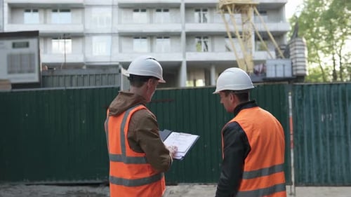 Dos profesionales de la construcción discuten un plan de trabajo de construcción en un sitio de construcción.