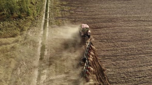 Tracteur puissant équipé d'une charrue cultivant le champ et soulevant d'énormes nuages de poussière brune suffocante