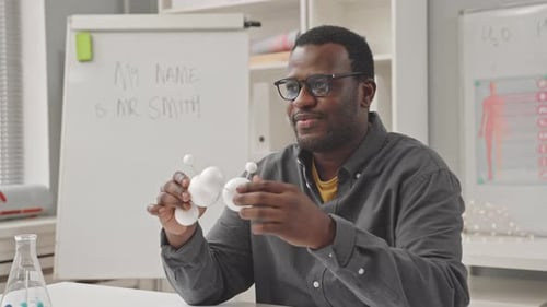 Science Teacher Explains Molecular Model at White Desk