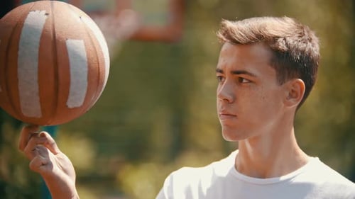 A Young Man Standing on a Sports Ground and Spinning the Basketball Ball on His Finger