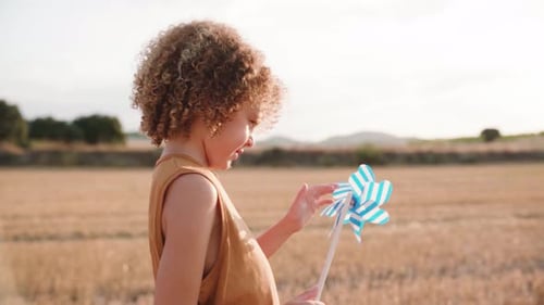 Close up shot of young boy with cool hairs spinning windmill standing in sunlight during sunset.