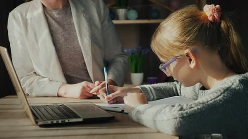 Child Writes in Notebook with Woman's Help