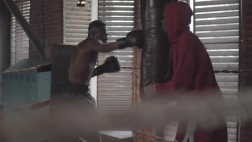 African Boxer Punching Bag and Trainer Holding at Fight Club