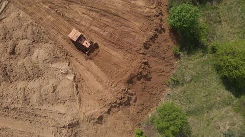 Aerial view of bulldozer flattening surface on further construction site