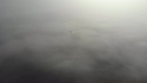 Birds eye view on tower crane in fog standing next to residential building.