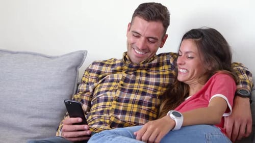 Smiling Couple Relaxing on Couch with Smartphone