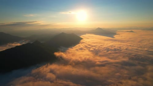 4K aerial view over mountain at sunrise in heavy fog. golden morning sunlight