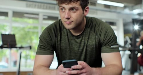 Athletic Man Relax Sitting and Texting Message on Smartphone at Gym Fitness