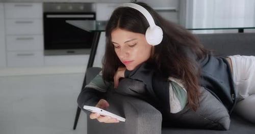 Brünette Mädchen im Teenageralter Musik hören Kopfhörer Entspannen auf dem Sofa SMS mit