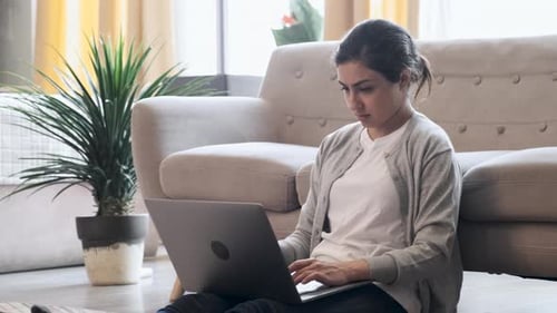 Self employed woman sitting on floor in cozy apartment and working online on project