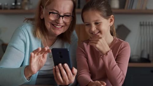 Grandmother and Granddaughter Laughing at Phone Indoors