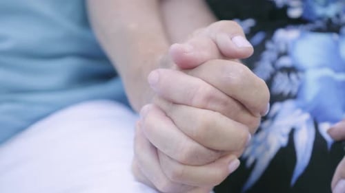 Hände eines reifen Mannes und einer reifen Frau, die auf der Bank sitzen