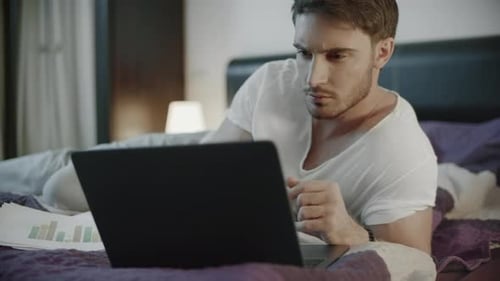 Man Works on Laptop in Bed